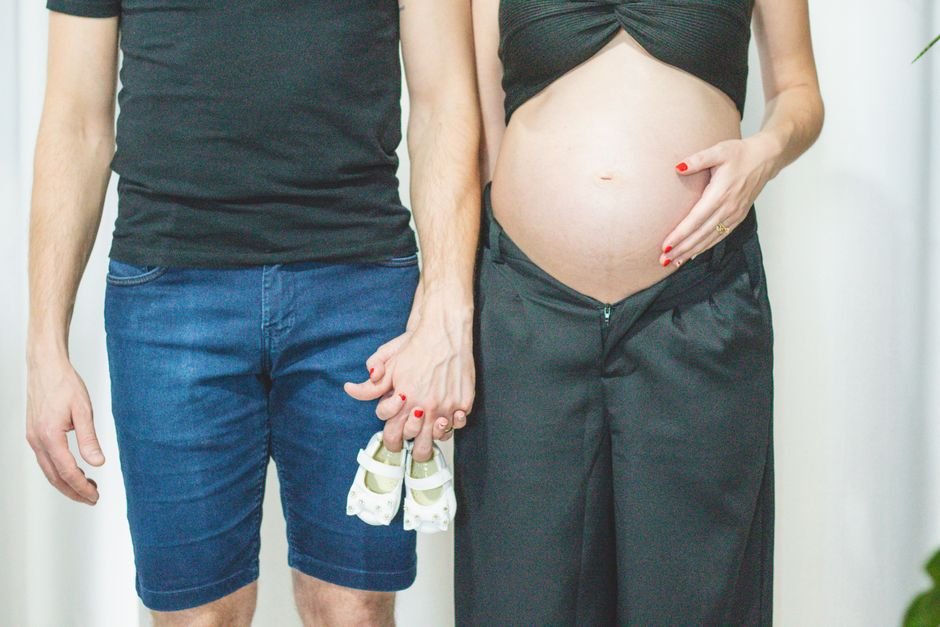 A pregnant couple holding baby shoes, symbolizing anticipation and parenthood.