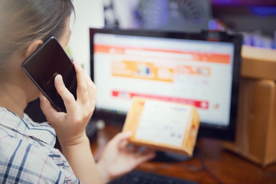 Woman multitasking by using a phone and checking an online purchase package at home.